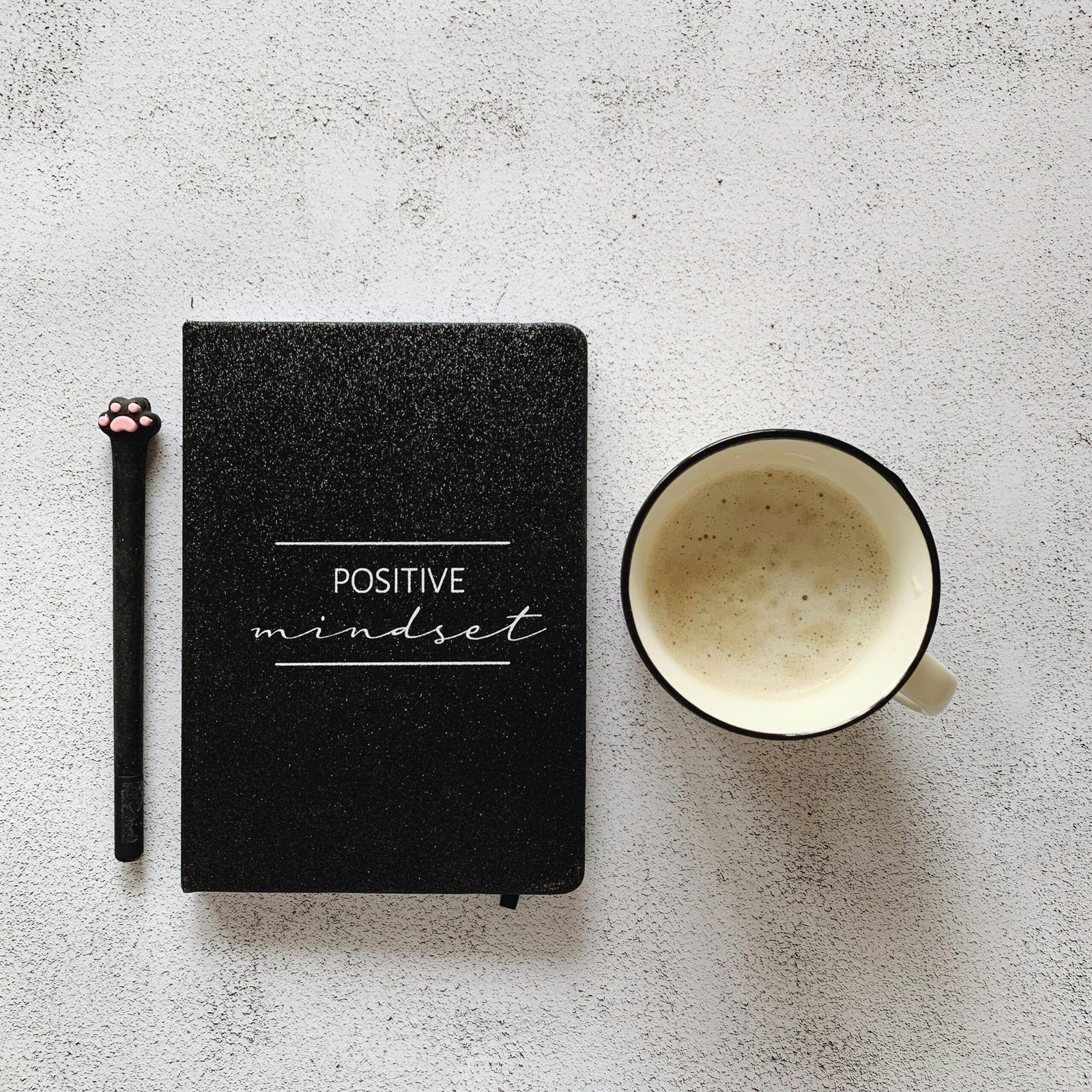 hand holding pen writing on a small white notecard with 'Today's Big 3:' visible at the top, beside a ceramic mug with steam rising