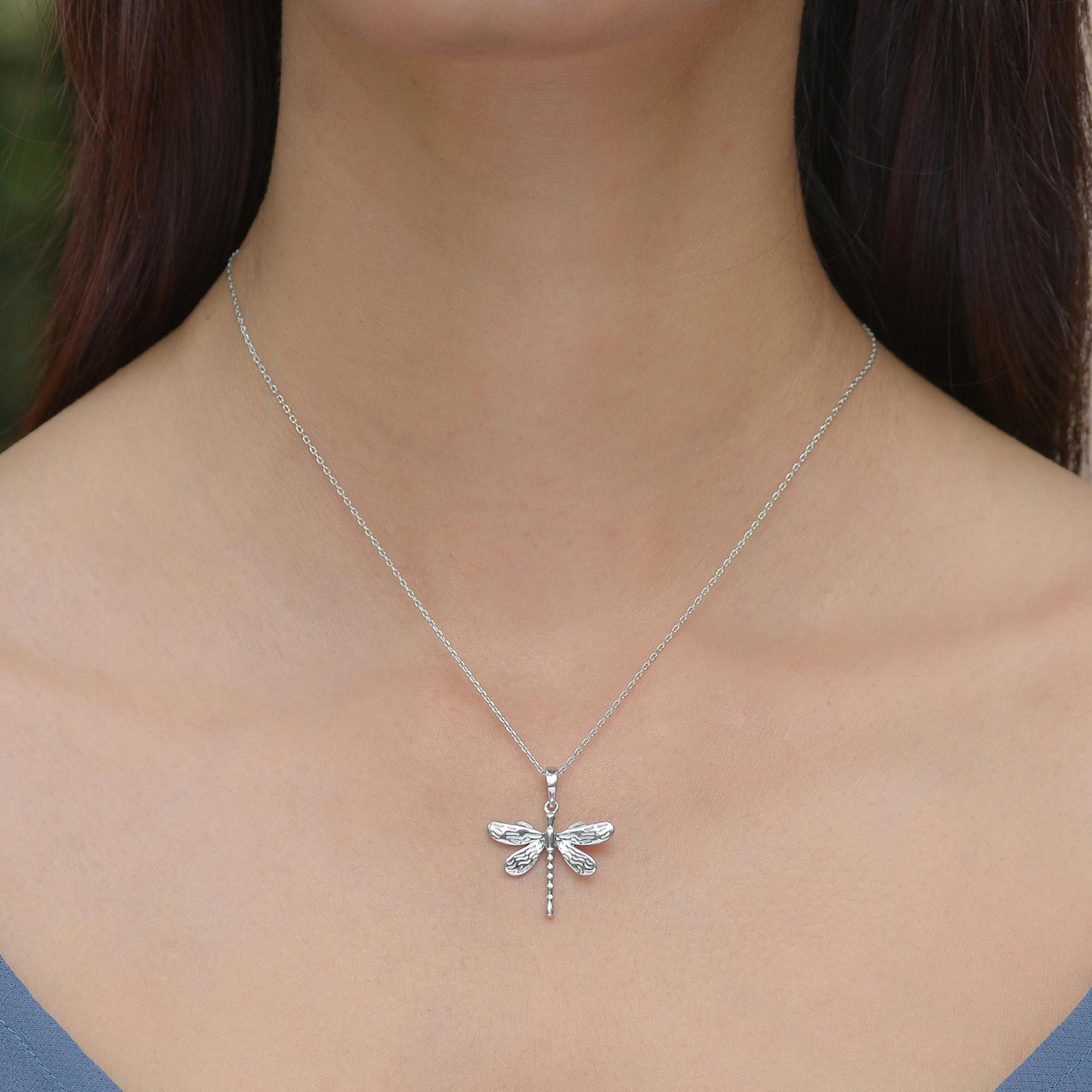 Close-up of a silver dragonfly necklace on a woman's neck, highlighting style and elegance.