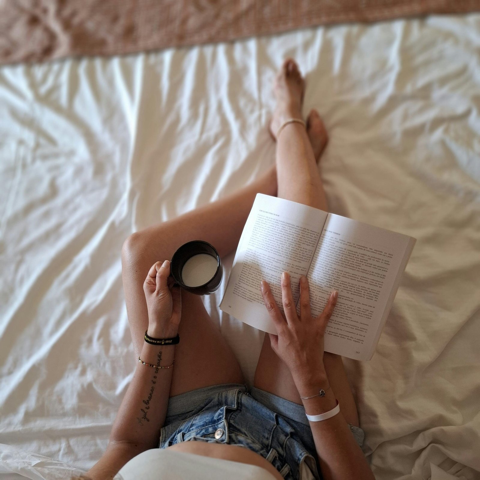 Woman reading a book while enjoying coffee in bed, capturing a relaxing and cozy morning vibe.