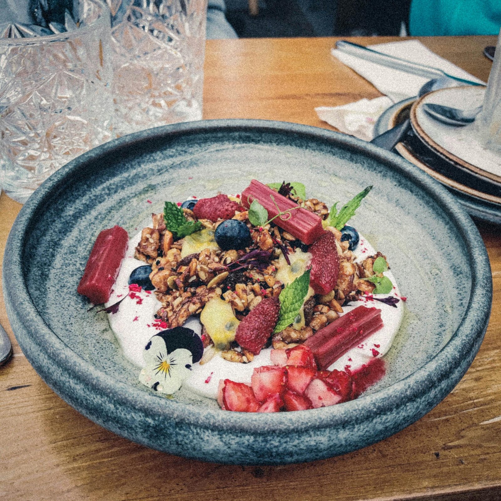 A vibrant breakfast bowl with granola, strawberries, mint, and yogurt on a wooden table.