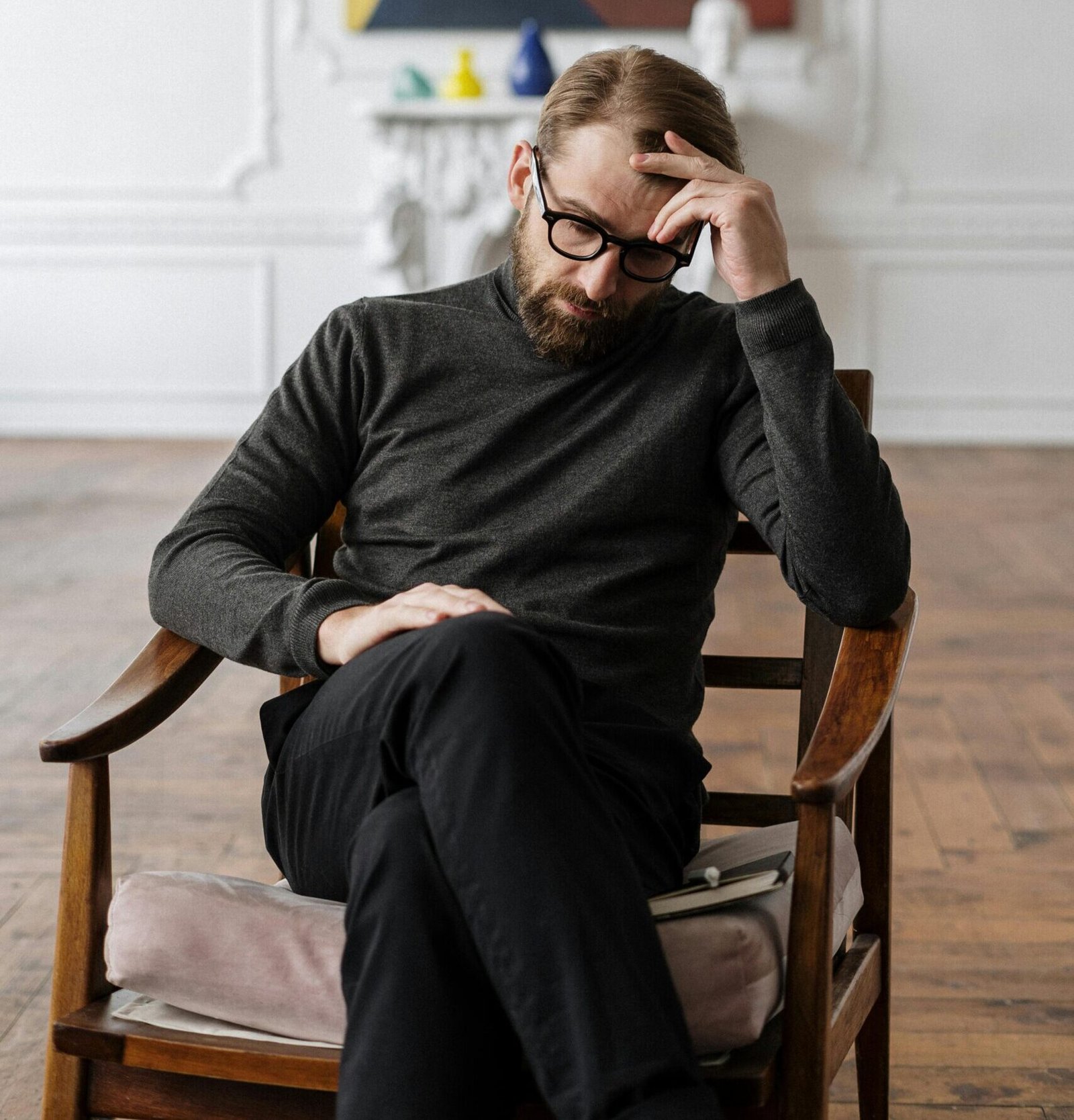 A man sits pensively in a chair, surrounded by abstract art in a stylish room.