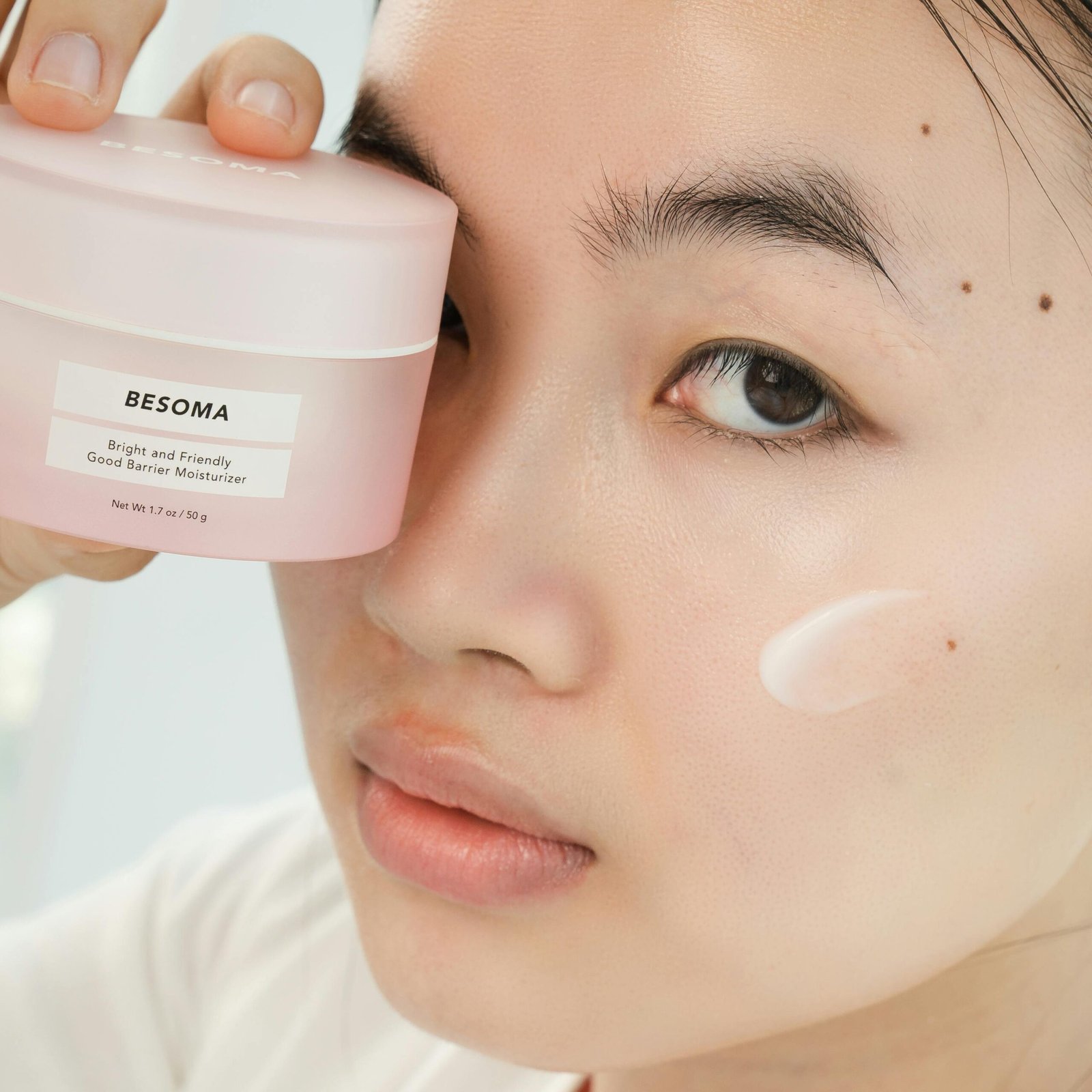 Close-up of an Asian woman holding a moisturizing cream, focusing on skincare.